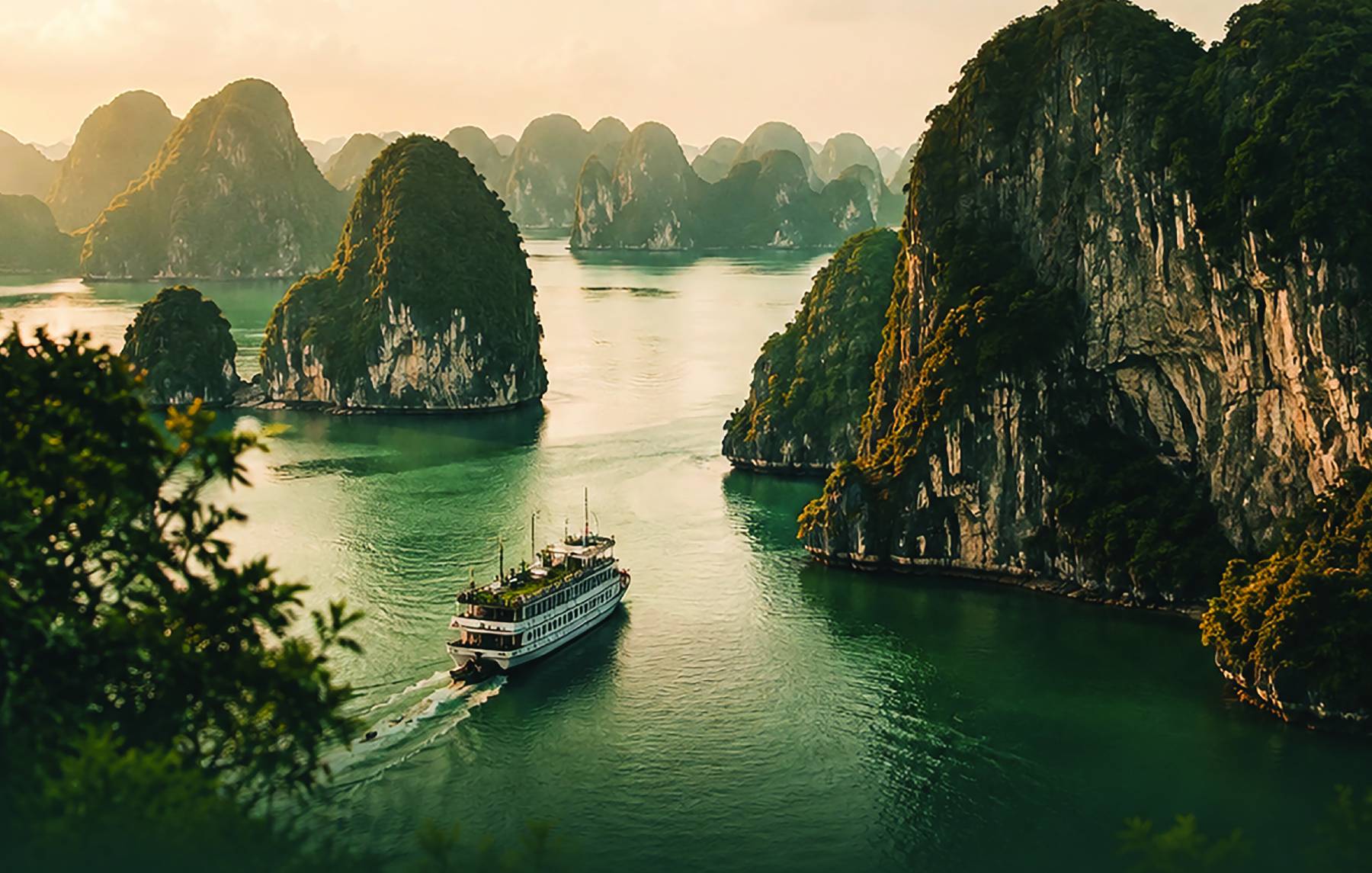 Cruise ship sailing between limestone islands in Ha Long Bay at sunrise